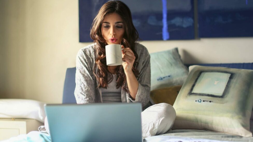 woman with cup of coffee, and working with an laptop on the bed